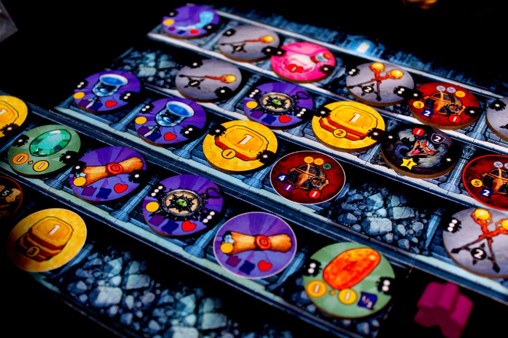 Close-up view of the game board for Satchel Quest, featuring various tokens, gems, and score indicators arranged on a colorful market layout.