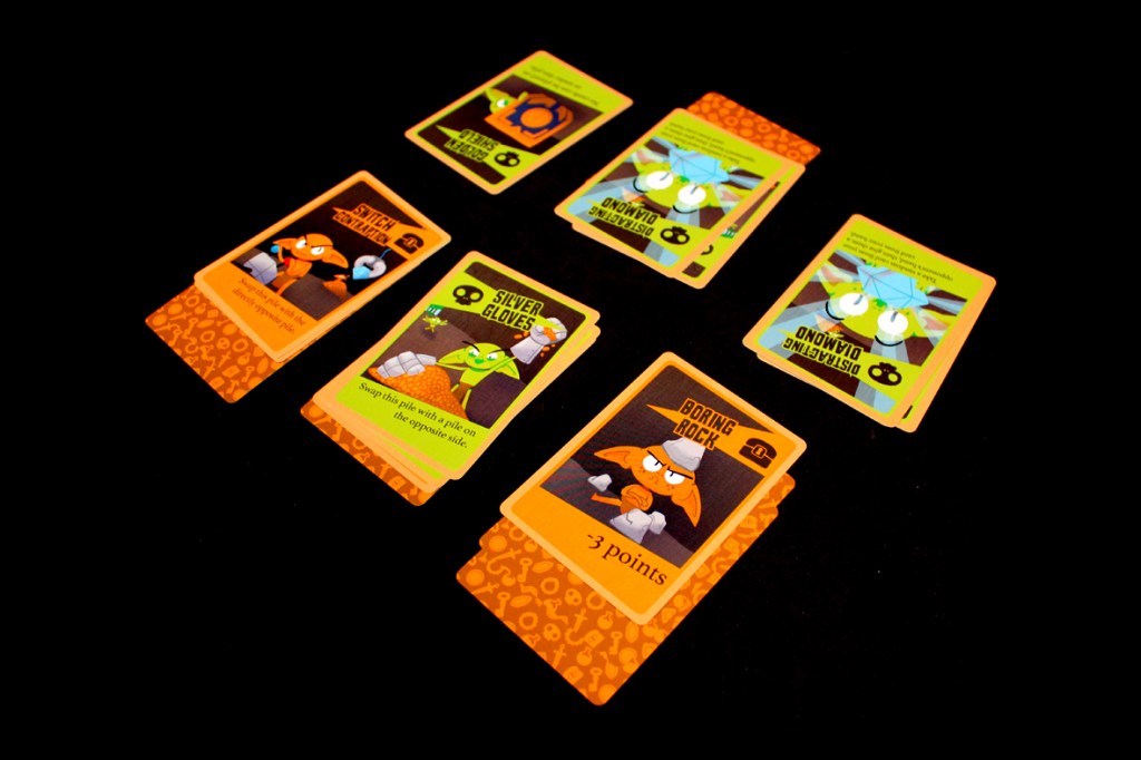 A collection of colorful game cards laid out on a black surface, featuring goblin characters and various gameplay instructions.