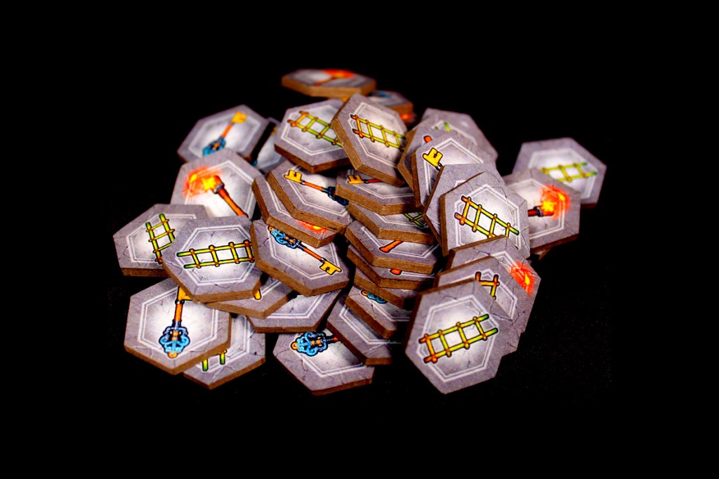 A pile of game tiles for Satchel Quest featuring various symbols like ladders and weapons, displayed against a black background.