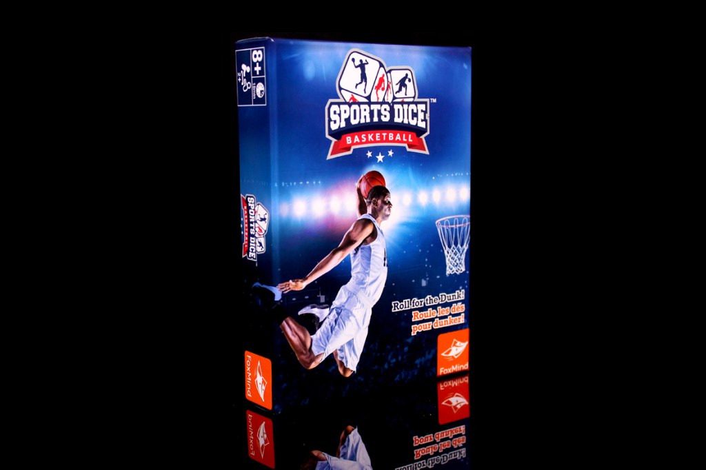 Box cover of Sports Dice: Basketball featuring a player jumping to dunk a basketball with graphics and text emphasizing the game's theme.