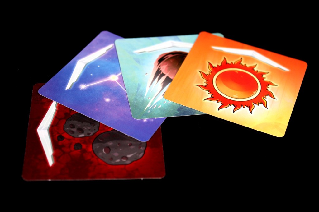 Four movement cards from the board game Crash & Grab, featuring colorful designs including an astrological sun, a comet, and asteroid fields, arranged on a black background.