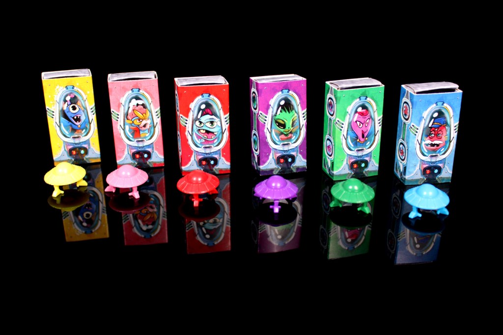 Colorful game boxes featuring cartoon alien characters displayed alongside matching small saucer pieces, reflecting a whimsical and fun art style.