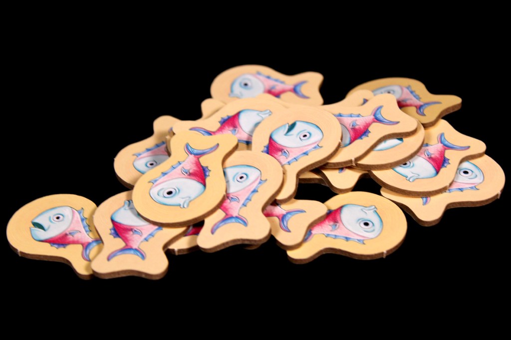 A pile of cartoon-style fish tokens used in the board game Push Push Penguin, featuring whimsical designs with exaggerated facial expressions.