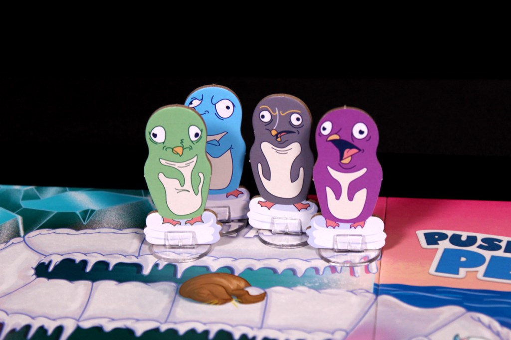 Four colorful penguin game pieces on a snowy game board for Push Push Penguin, featuring comical expressions.