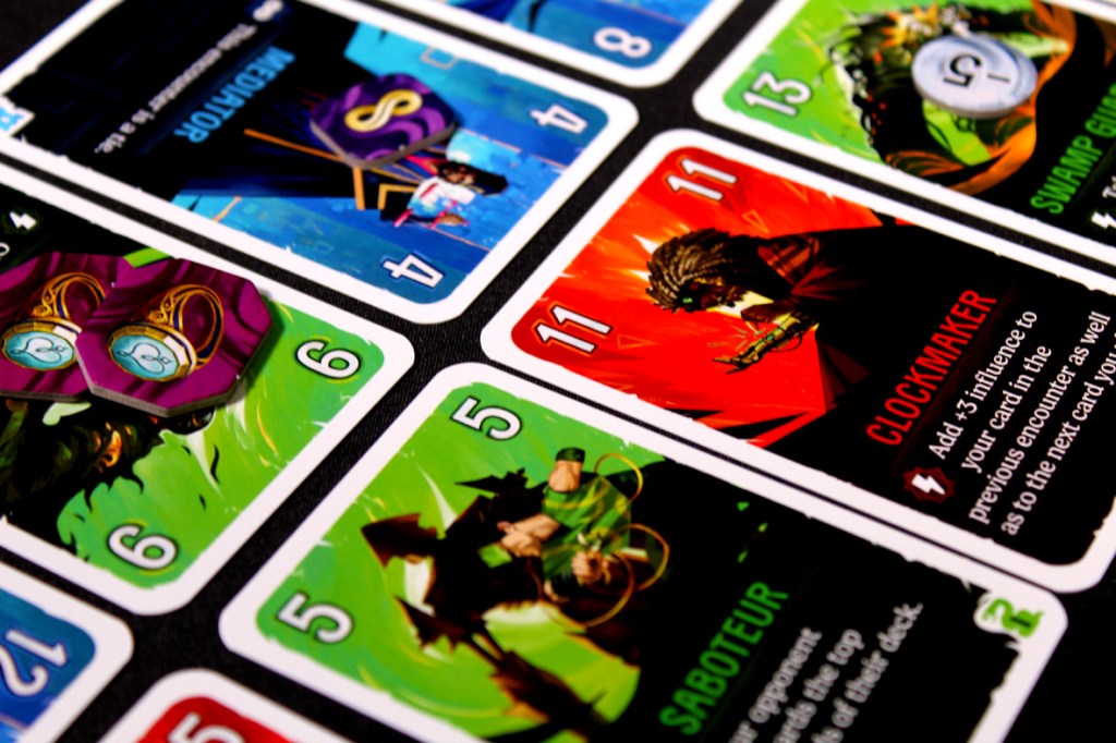 Close-up shot of colorful game cards from Duel for Cardia, showcasing various cards with unique abilities and values, including characters like Clockmaker and keywords like Saboteur.