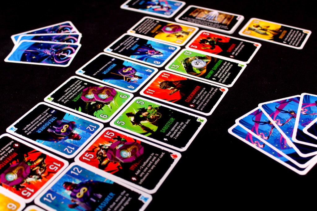 A tabletop game setup featuring various colorful cards laid out on a black surface, with some cards in a stack on the left side. The cards display different character abilities and values.