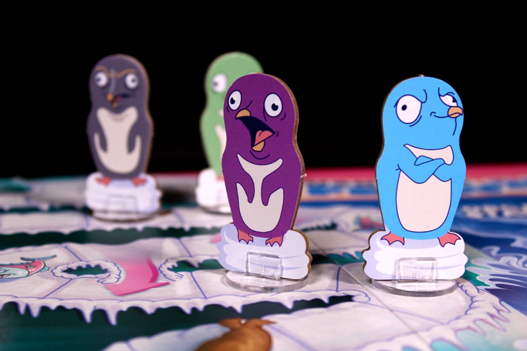 Close-up of colorful penguin game pieces on a board game, featuring unique designs and expressions, with an icy game board in the background.