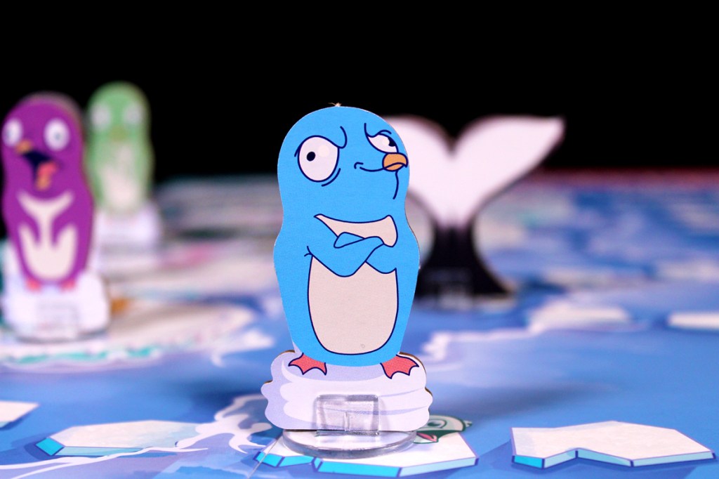 A blue penguin game piece with an expressive face, standing on an ice platform, surrounded by other colorful penguin pieces and a background featuring an ocean-like board.