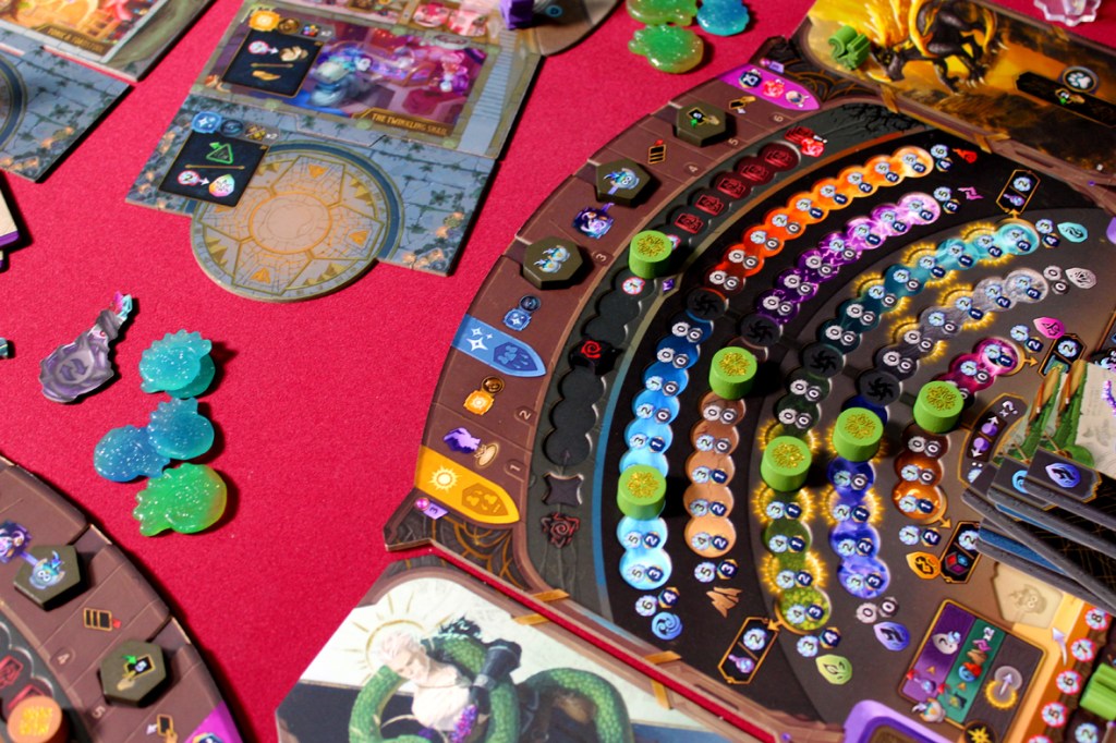 A detailed tabletop game setup displaying colorful components, including player boards, tokens, and potion ingredients on a pink background.