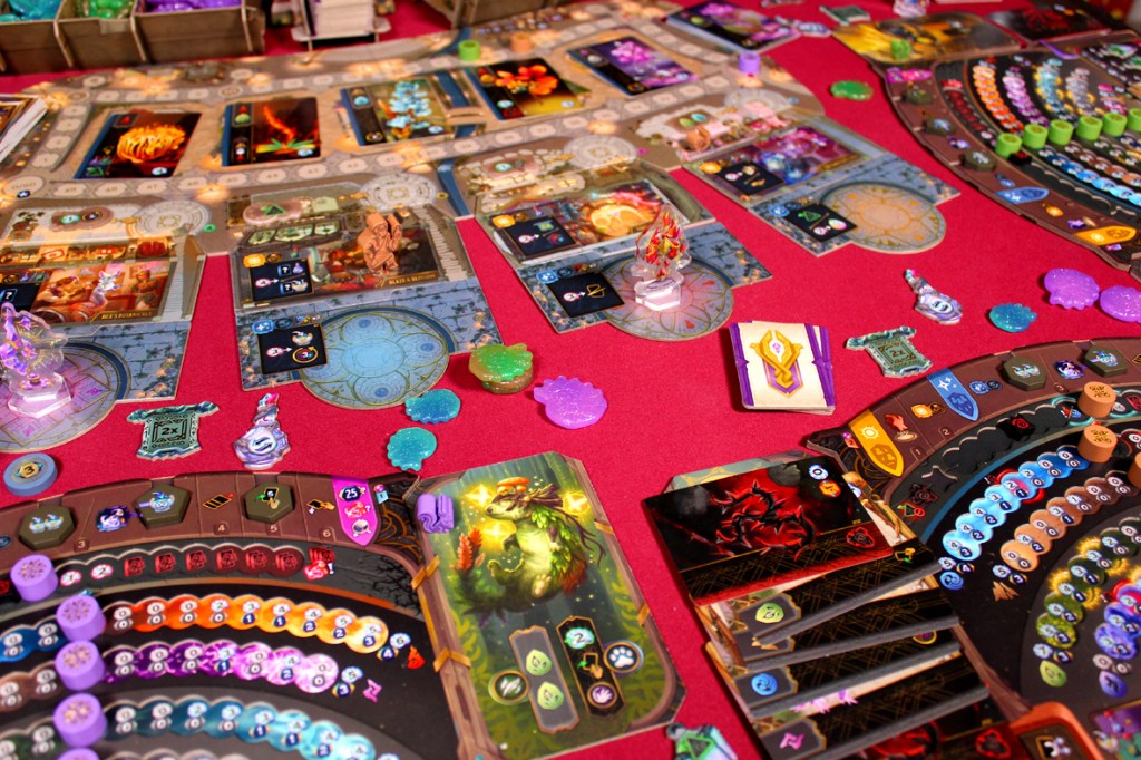 A colorful board game setup featuring various potion cards, character tokens, and resource markers, laid out on a red tablecloth.