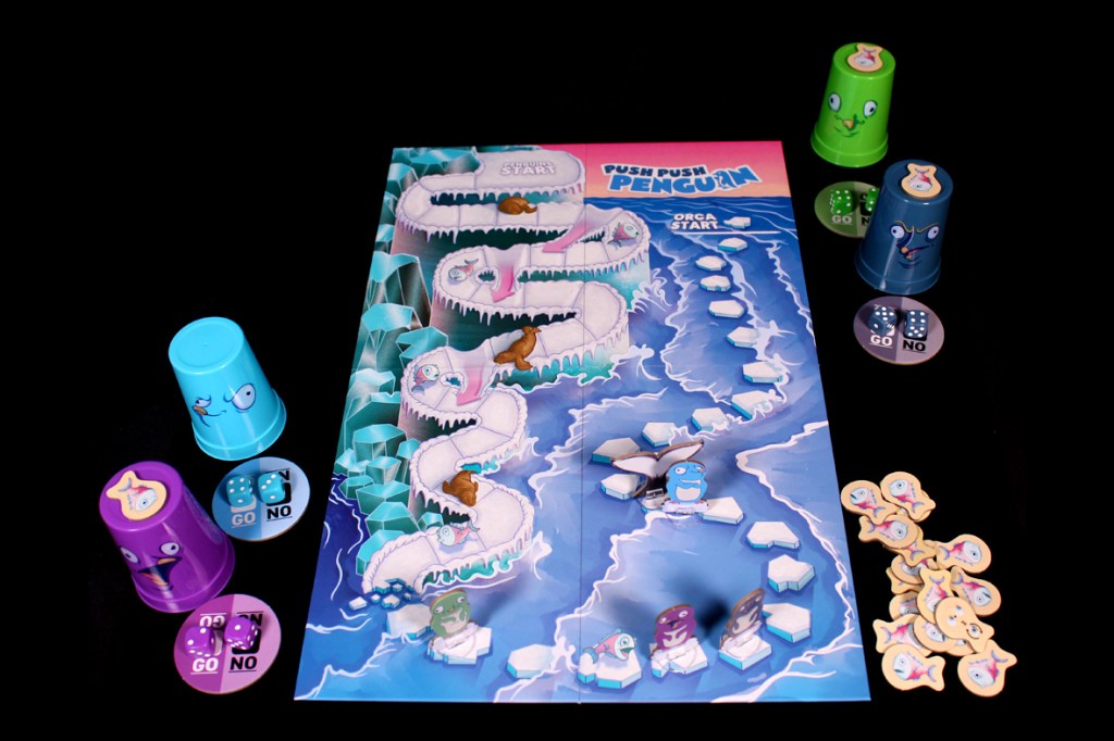 A colorful board game setup for 'Push Push Penguin,' featuring a game board with an icy path, various penguin cups, dice, and fish tokens laid out for players.
