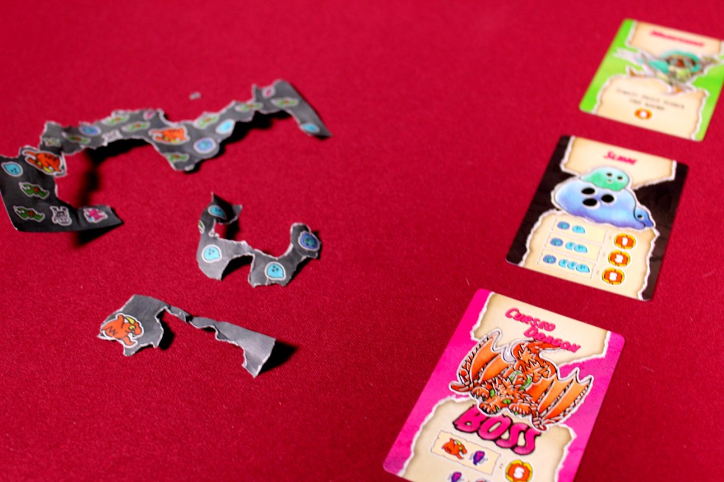 Torn game pieces with colorful illustrations alongside game cards on a red surface.