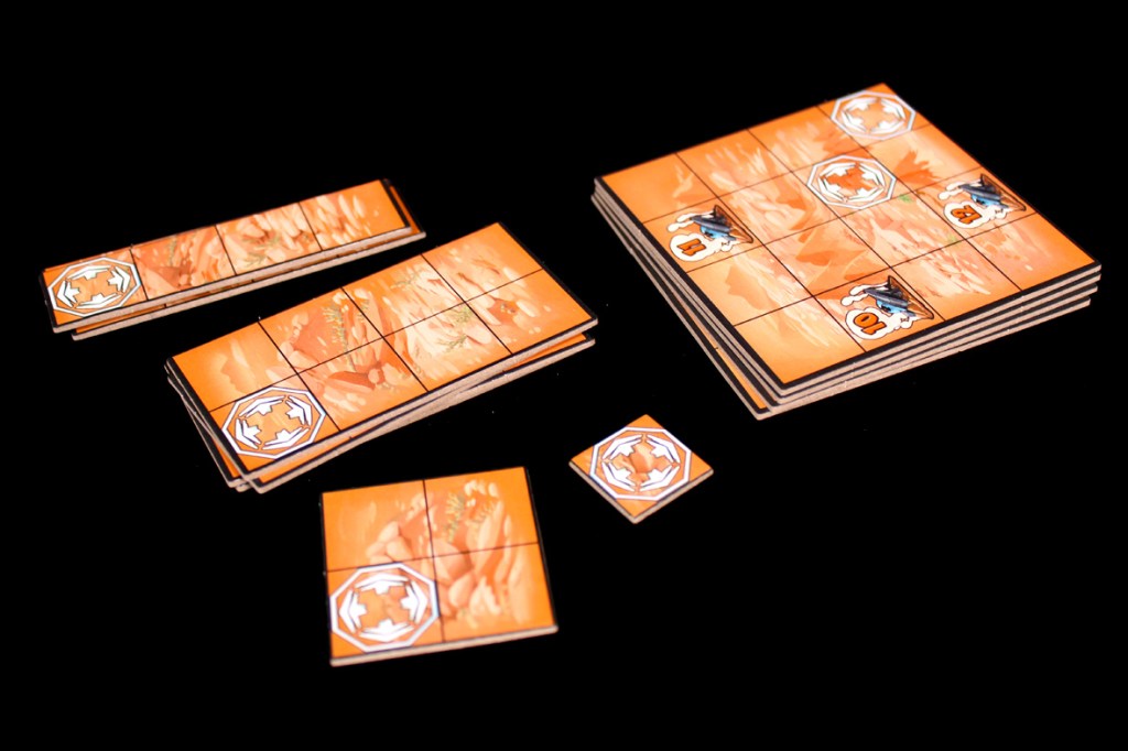 An assortment of game tiles in varying sizes featuring an orange design with directional icons and numbers, arranged on a black background.