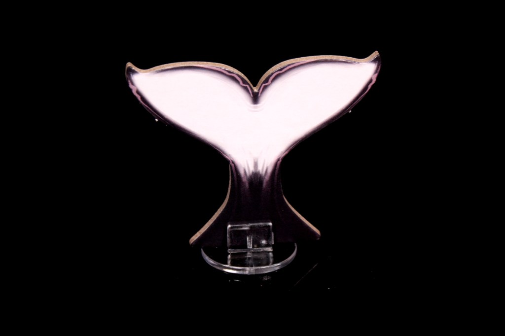 A whale tail figure displayed on a clear stand against a black background.