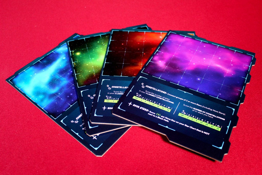 A set of scoring boards for the board game Twinkle Twinkle, featuring colorful star-filled backgrounds and grid patterns, displayed on a red surface.