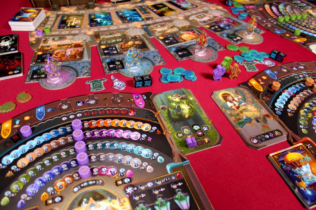 A top-down view of the board game Mercurial: Alchemia, showcasing various colorful game components, including cards, player boards, potions, and tokens on a red game mat.
