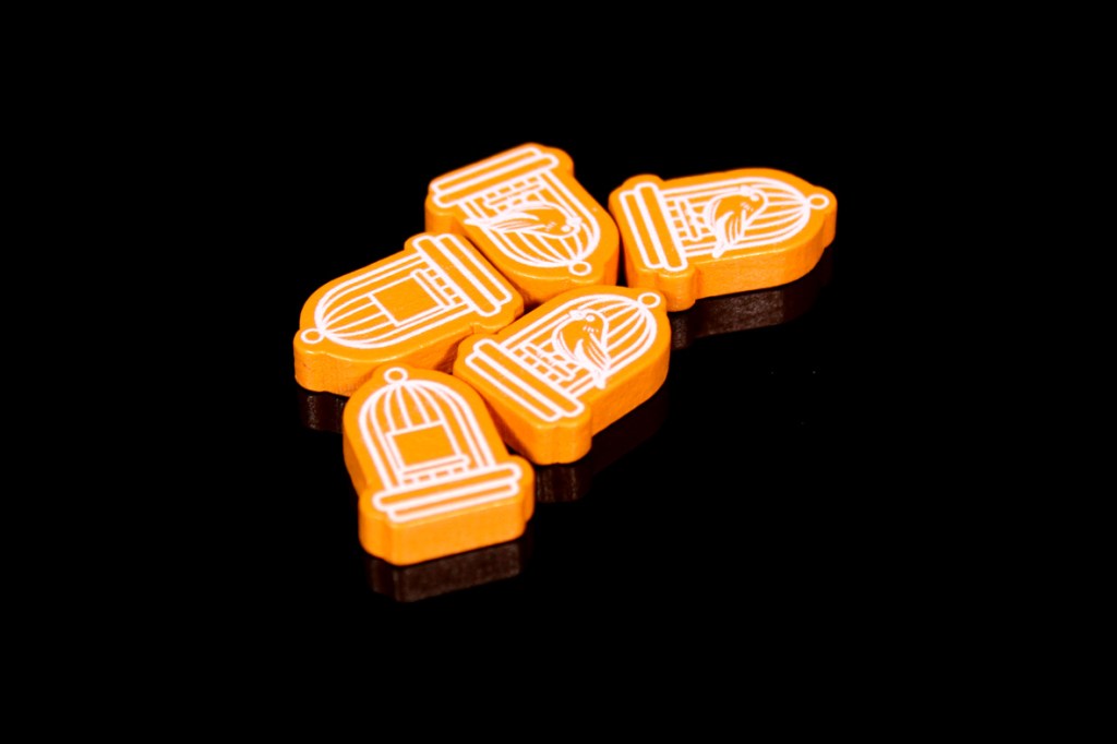 Five orange tokens shaped like birdcages featuring white designs, placed on a black background.