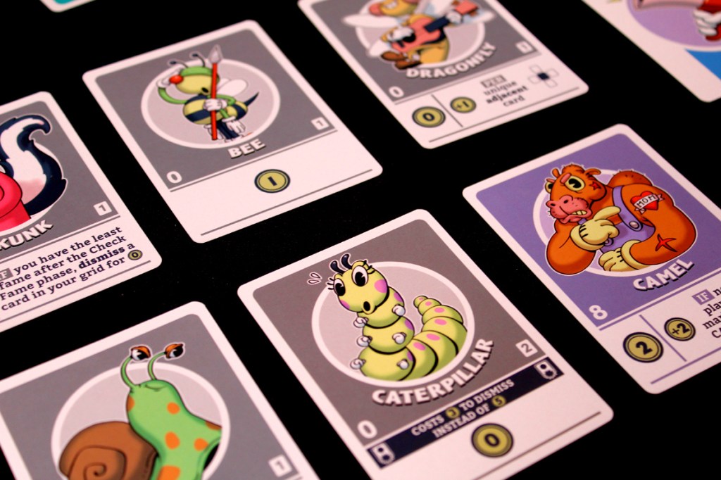 A close-up of various character cards from the board game FlipToons, featuring a skunk, bee, caterpillar, dragonfly, and camel, each with unique attributes and artwork.