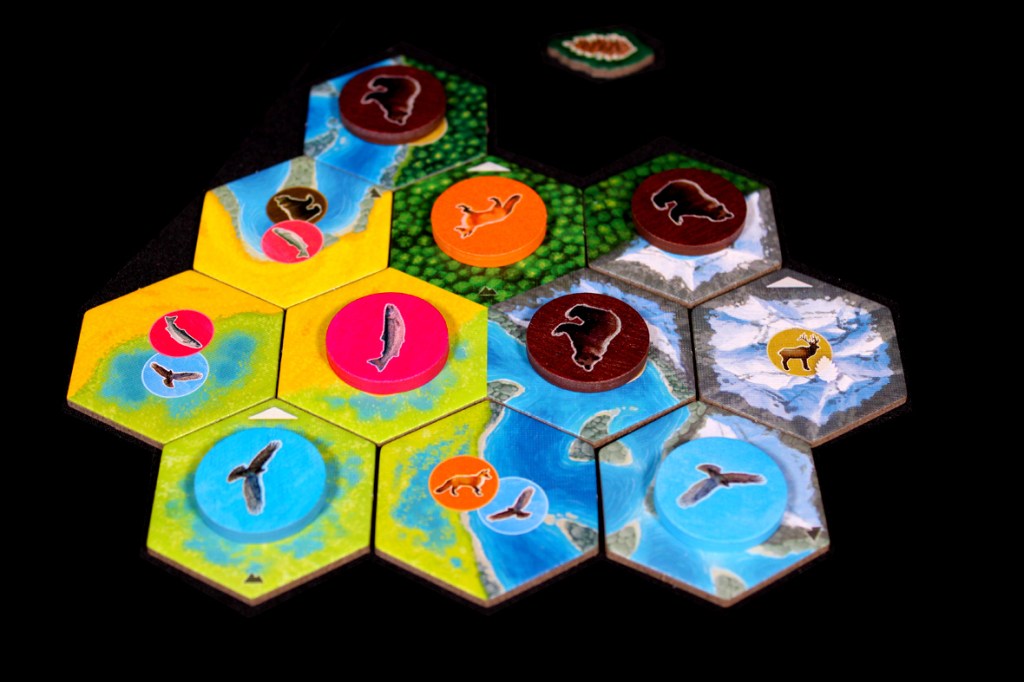 A game board for Cascadia: Landmarks displaying various hexagonal tiles featuring illustrations of wildlife such as bears, salmon, and birds, along with rivers and green habitats.