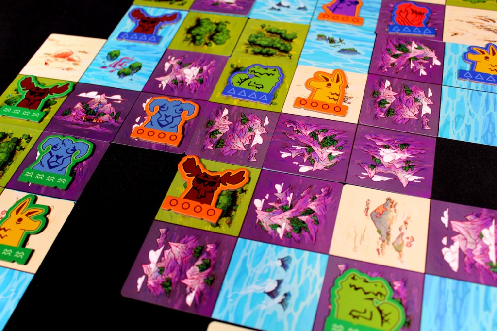 A tabletop game board for Oddland, featuring colorful cards representing various landscapes and strange animal tokens placed on the grid.