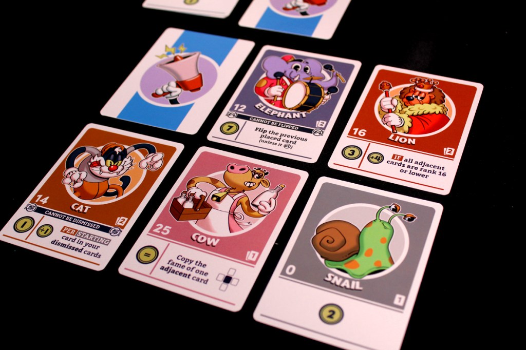 A flat lay of several character cards from the game FlipToons, featuring illustrations of a cat, cow, elephant, lion, and snail, each displaying their rank and special abilities.