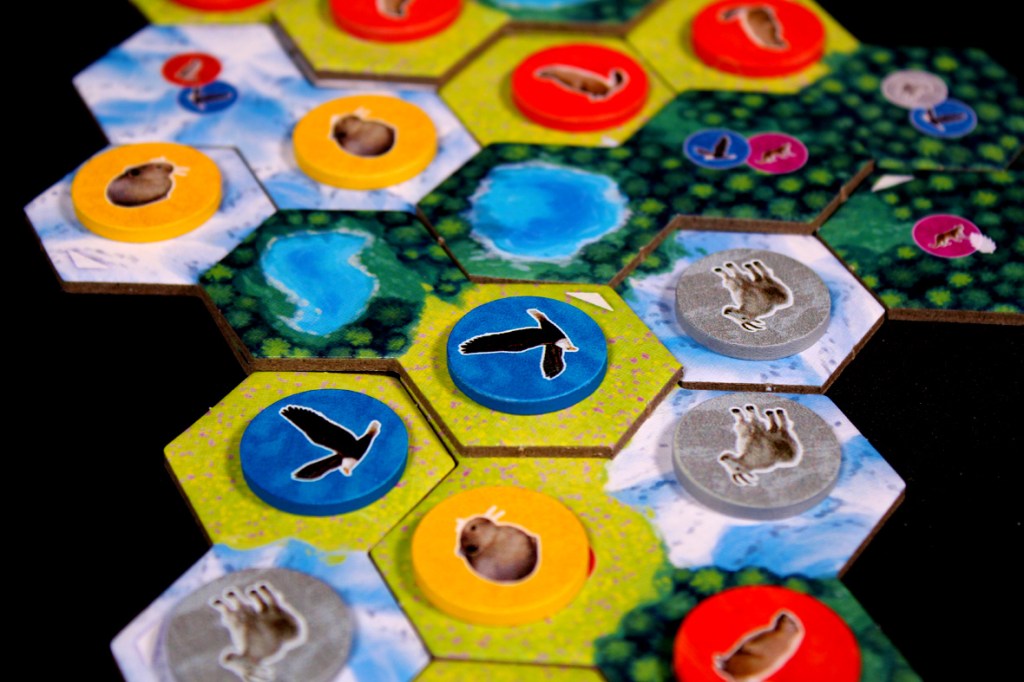 Colorful game board with hexagonal tiles depicting lakes and various wildlife tokens including birds and animals, designed for the game Cascadia: Alpine Lakes.