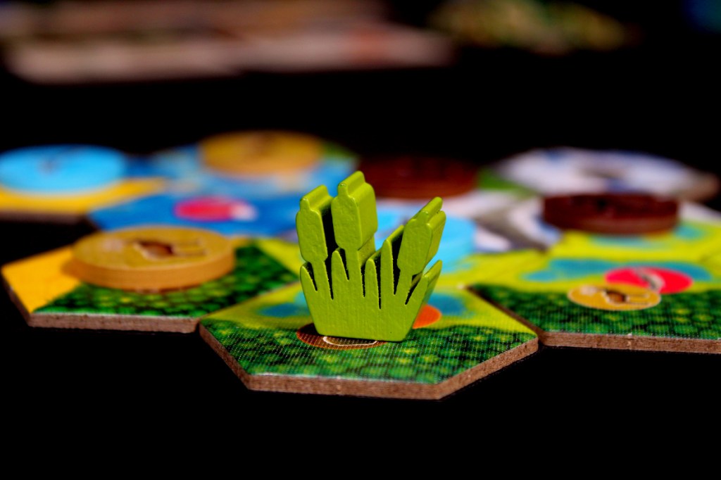 Close-up of game components from Cascadia: Landmarks, featuring a green wooden piece resembling grass and hexagonal tiles that form part of the game board.