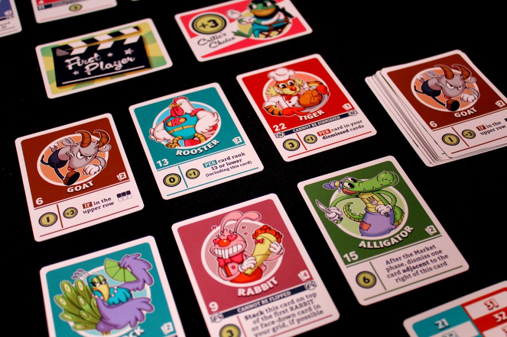 An assortment of cartoon character cards from the game FlipToons, featuring characters like Goat, Rooster, Tiger, Rabbit, and Alligator, displayed on a black surface alongside the First Player and Critic's Choice cards.