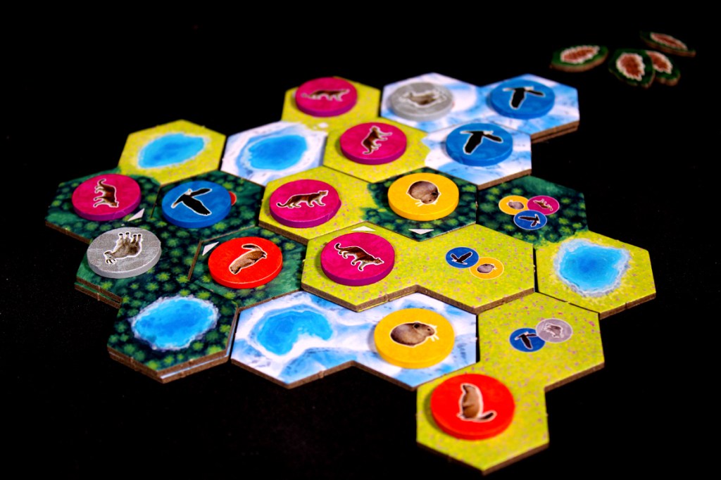 A board game layout featuring hexagonal tiles with illustrations of lakes and various animal tokens in vibrant colors.