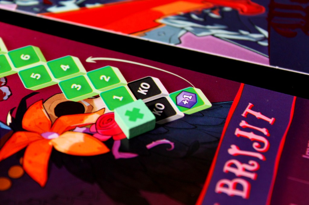 Close-up of a board game setup showing character tracking tokens, including health points and KO markers, against a colorful game backdrop.