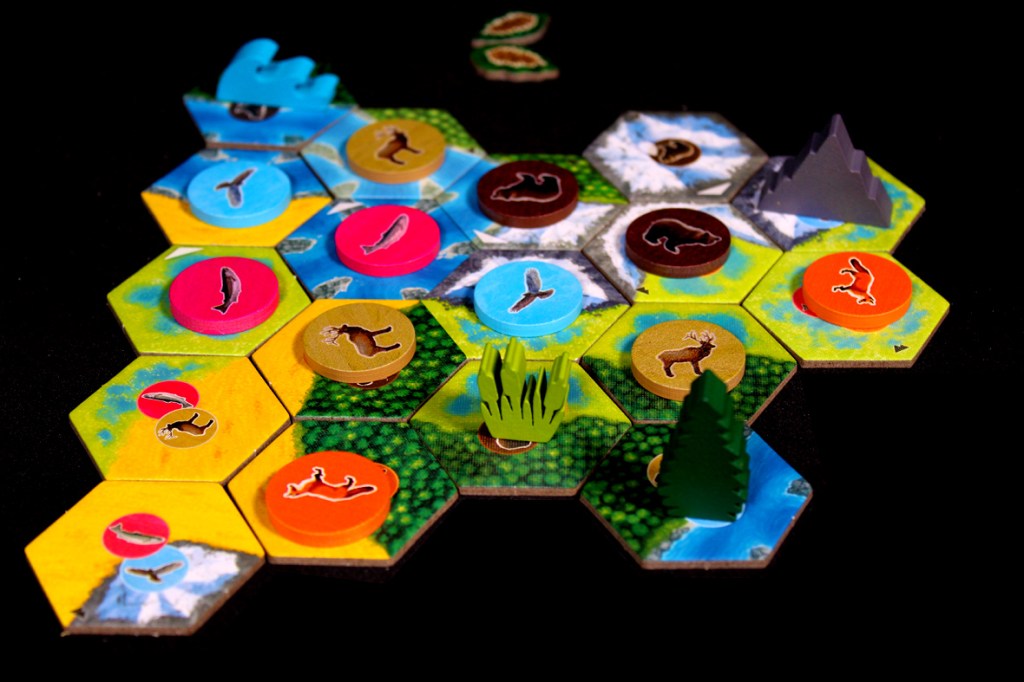 Colorful board game setup with hexagonal tiles representing different habitats and animal tokens placed on them.