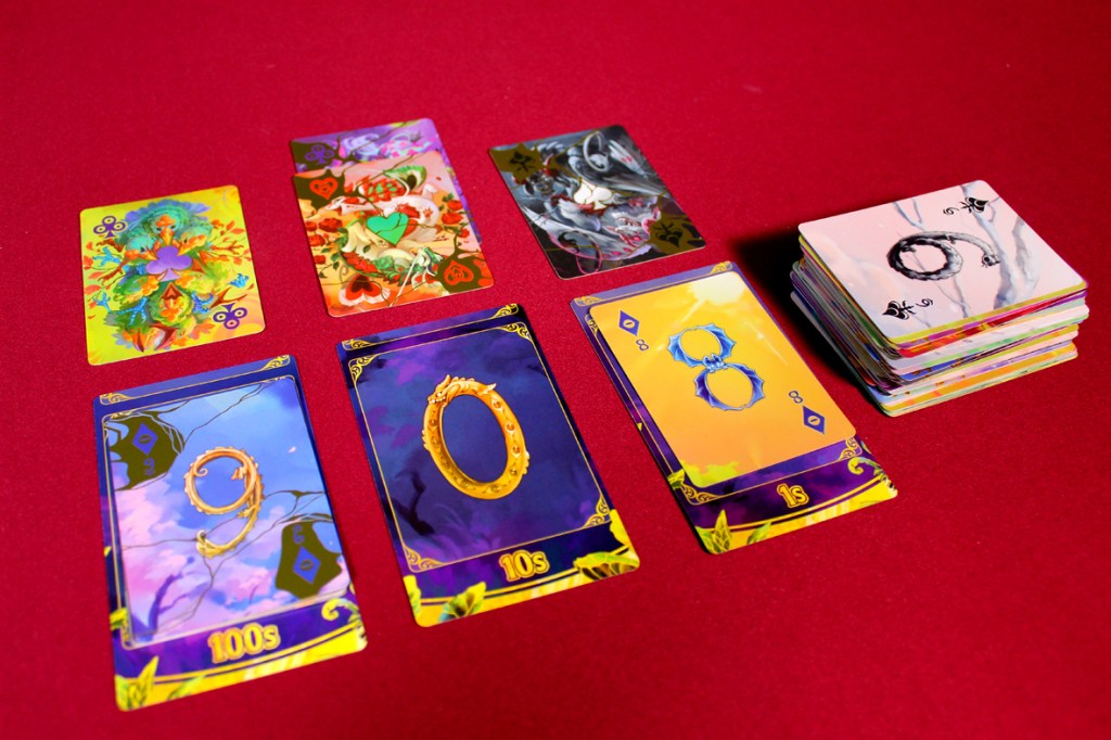 A layout of playing cards on a red surface, featuring colorful illustrations on the top cards, including a character card and a suit icon, alongside number cards depicting 8, 9, and a placeholder for 1, with a stack of additional cards in the background.