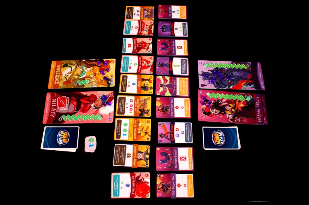 A table set up for the board game Tag Team, featuring character cards, ability cards, and tokens displayed in an organized manner. Various characters from history and mythology are represented, showcasing their health and abilities.
