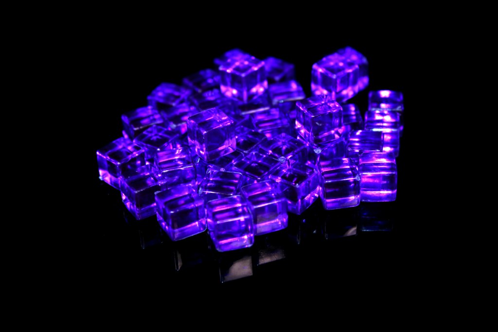 A pile of translucent purple game tokens arranged on a reflective surface, set against a black background.