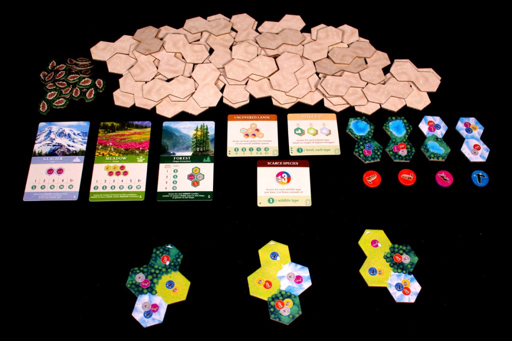 An assortment of hexagonal game tiles, wildlife tokens, and scoring cards laid out for the board game Cascadia: Alpine Lakes.