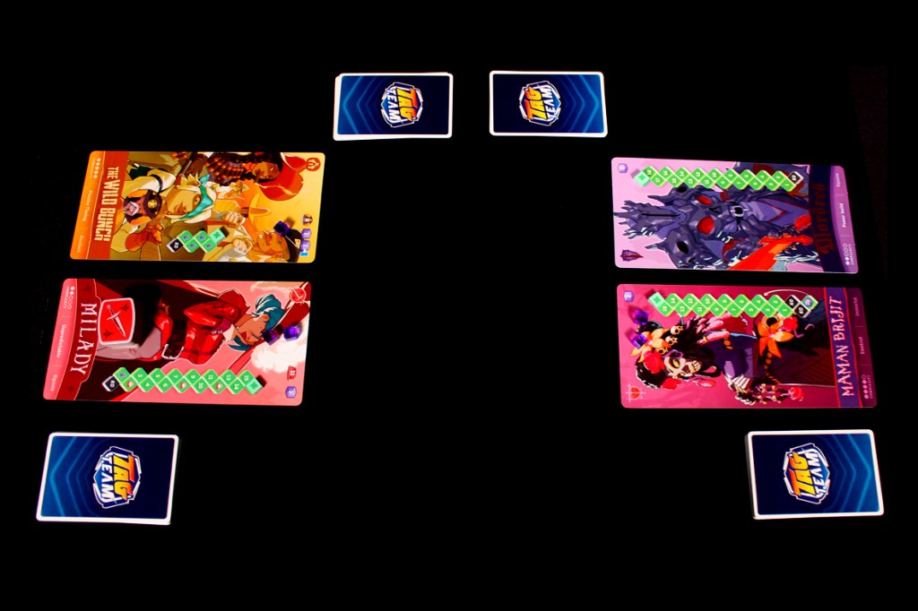 A bird's-eye view of a tabletop game setup for Tag Team, showcasing character cards on opposite sides and a central game logo.