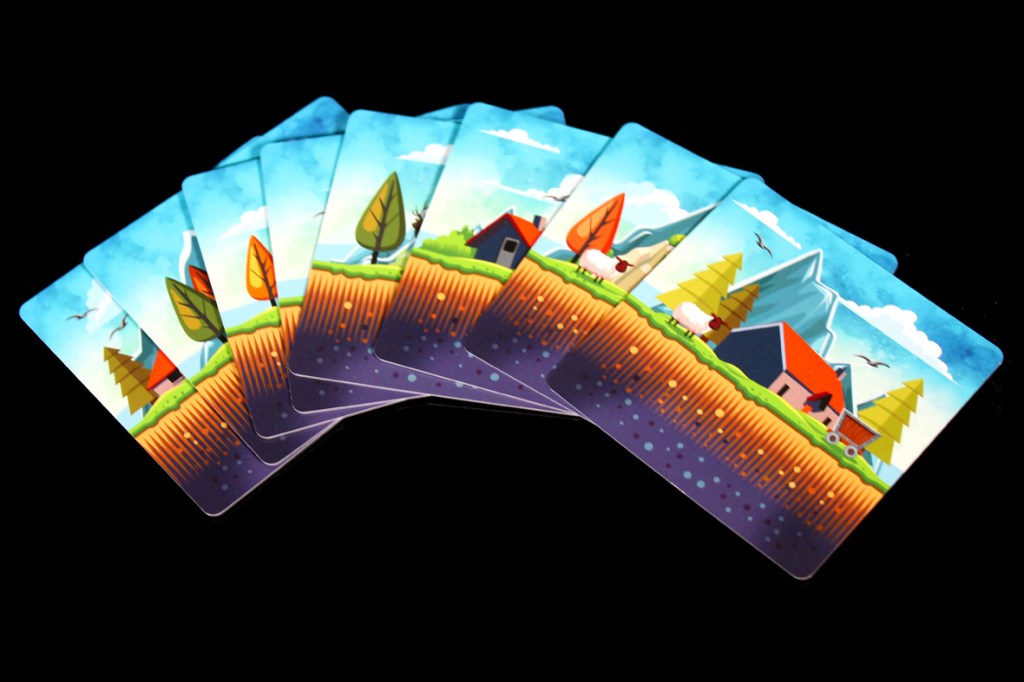 A set of game cards featuring a colorful illustration of a rural landscape with trees, houses, and mountains.