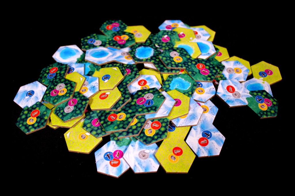 A pile of hexagonal tiles for the board game 'Cascadia: Alpine Lakes,' featuring various designs depicting lakes, greenery, and wildlife tokens.