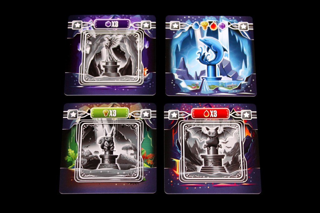 Four game cards showcasing different statues with various colors and symbols, representing elements in a board game.