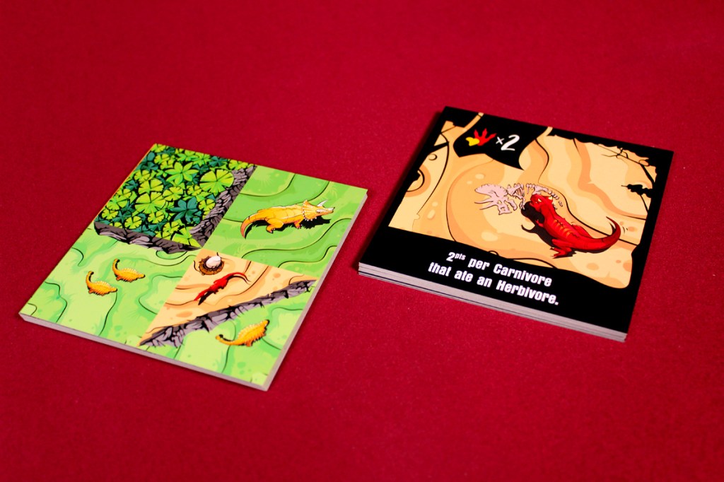 A dinosaur game card showing land and goal elements, with vibrant illustrations of dinosaurs, foliage, and a scoring rule on a bright red background.