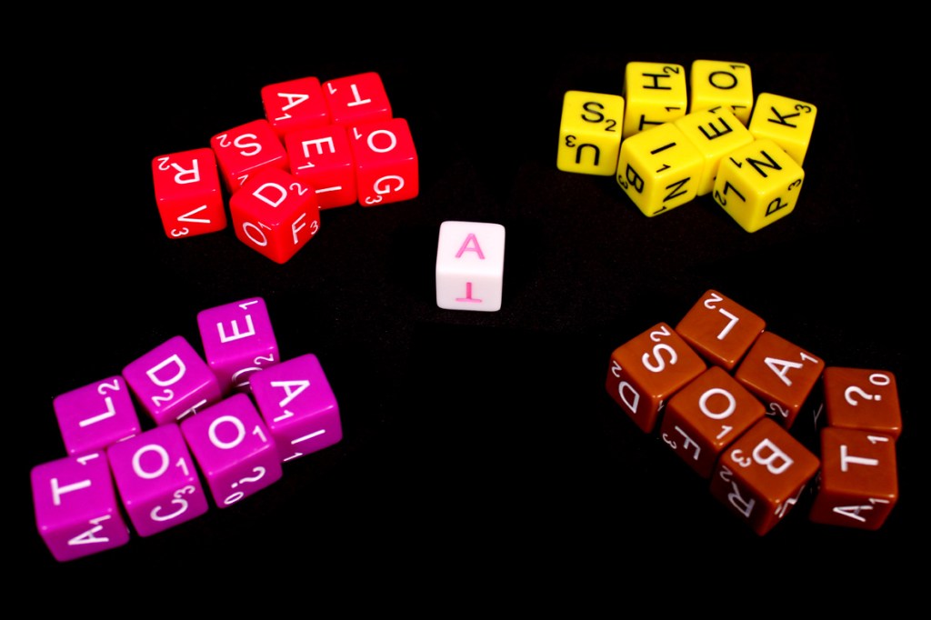 Colorful dice in different shapes and sizes arranged on a black background, including letters and symbols used for playing the game Dice Words.