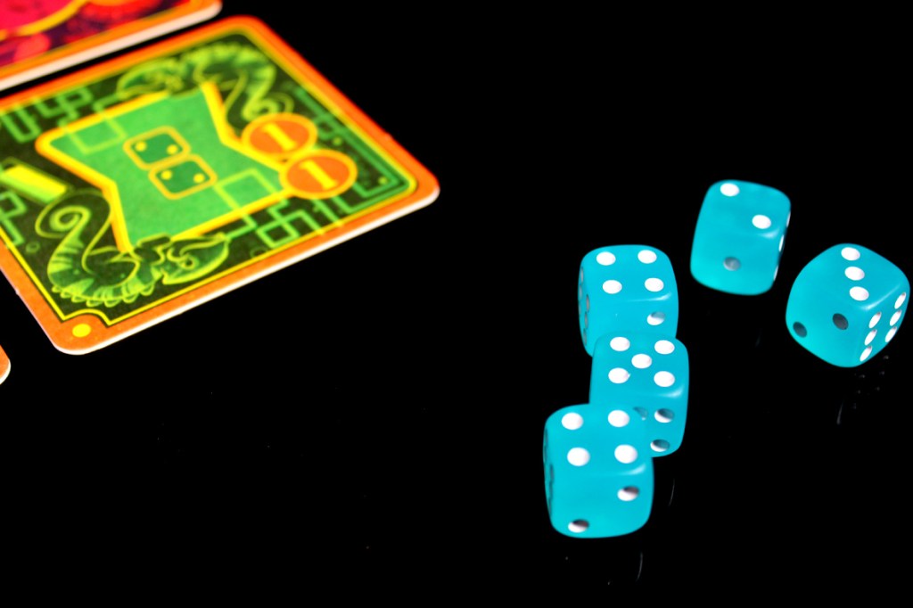 Close-up of turquoise dice arranged next to colorful game coasters on a black background.