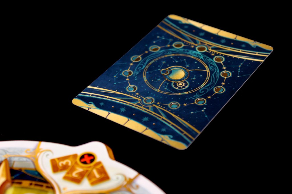 A detailed card from the board game 'Take Time,' featuring a mystical celestial design with a circular motif and various geometric patterns against a dark background.