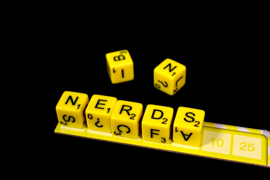 Yellow dice with letters spelling 'NERDS' on a black background, accompanied by a scoring board.