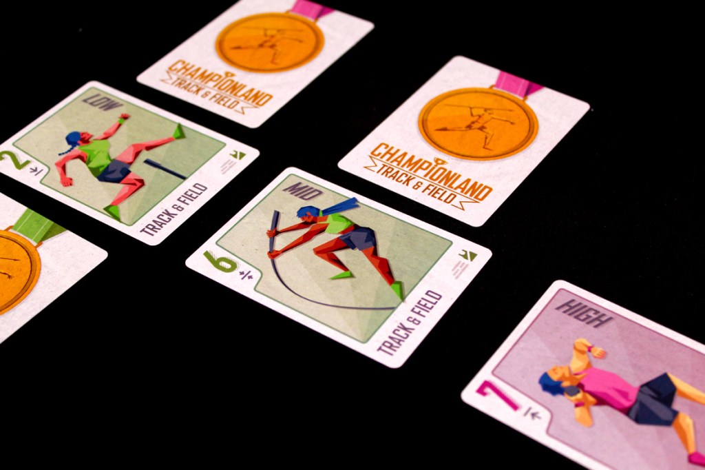 A display of Championland: Track & Field game cards featuring three cards labeled 'Low,' 'Mid,' and 'High,' alongside a medal with the game's title on a black background.