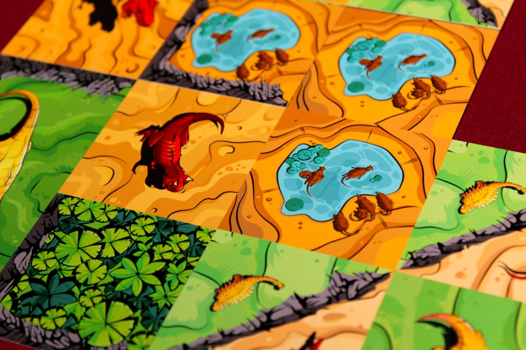 A close-up view of several colorful game cards displaying various terrains, including ponds, sandy areas, and greenery, with illustrations of dinosaurs and water features.