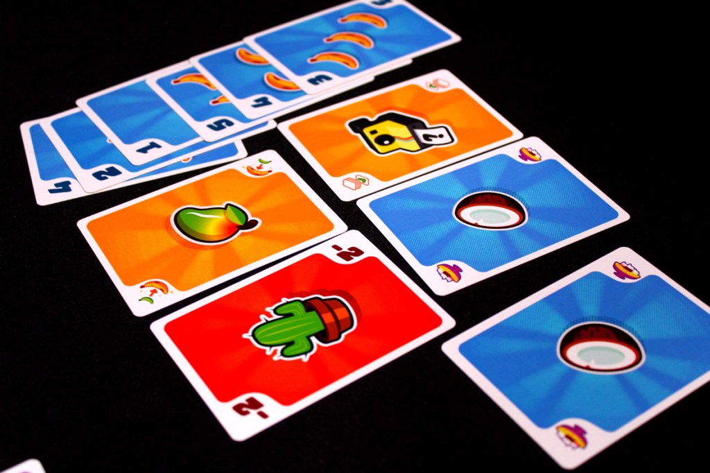 An array of colorful game cards featuring illustrations of bananas, cacti, and other fruit-themed designs, arranged on a dark surface.
