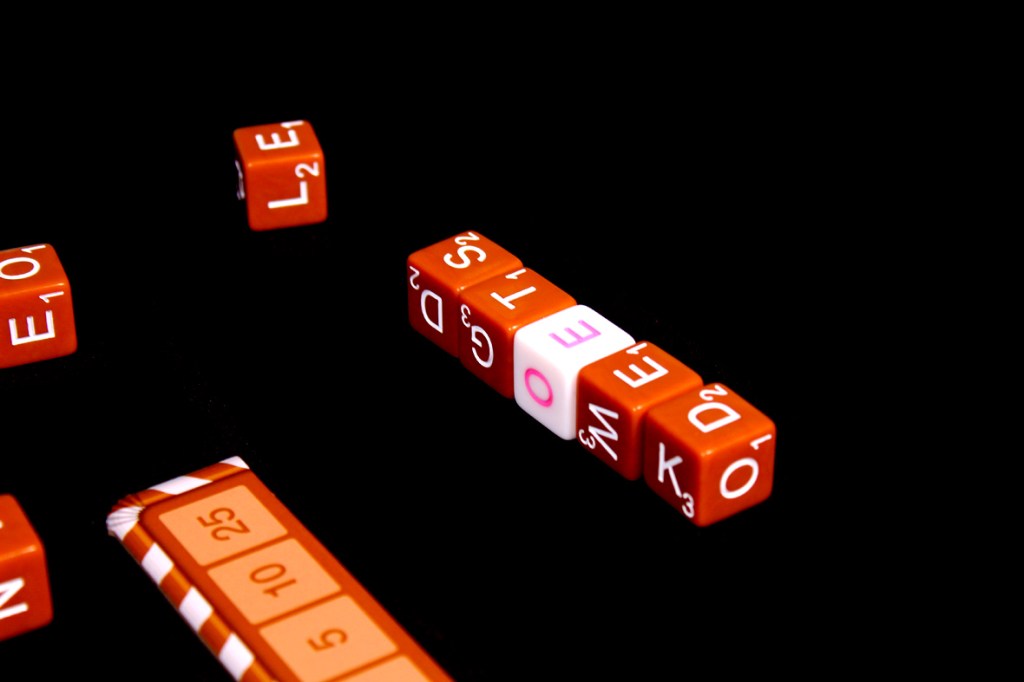 Close-up of orange and white letter dice, displaying various letters, arranged on a black background with a scoring board.