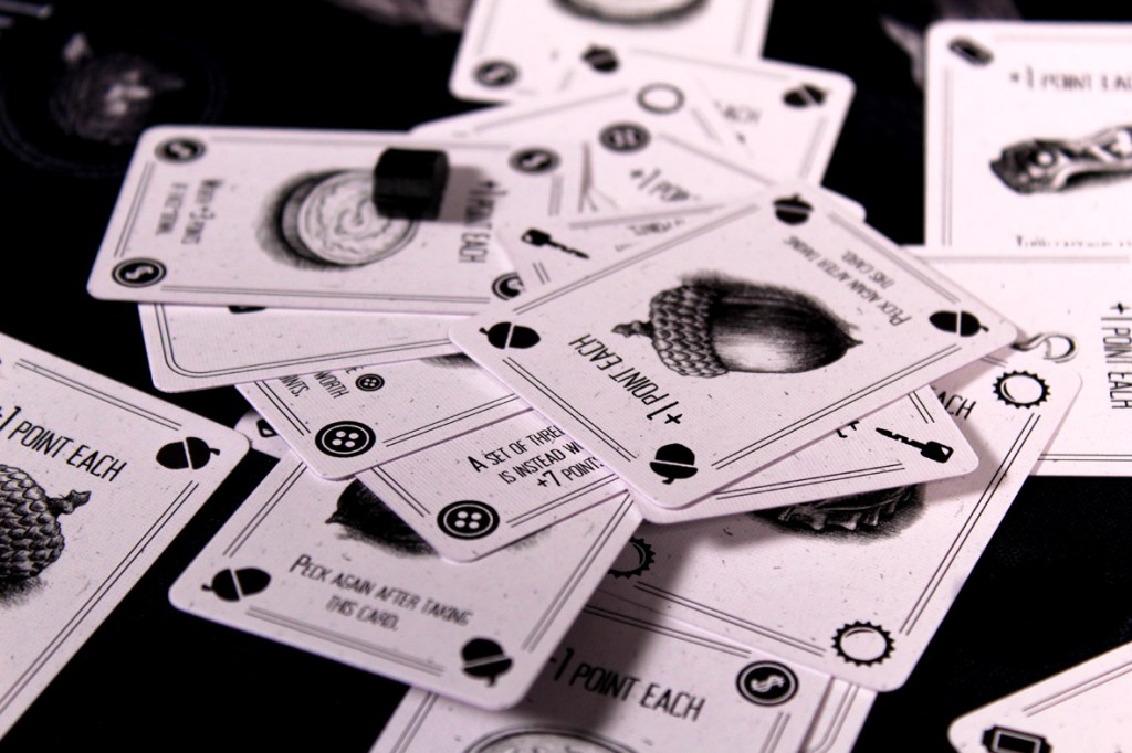 A collection of cards from the game Corvids, featuring various illustrations and scoring instructions, spread out on a dark surface.