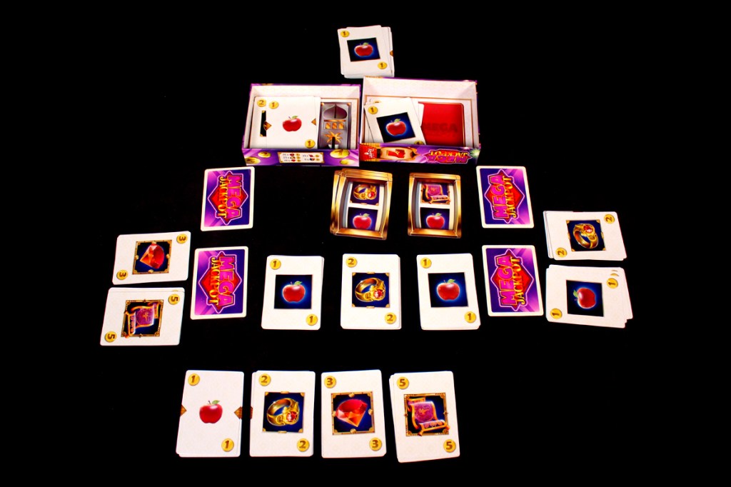 A table setup of the board game 'Mega Jackpot' featuring various playing cards, money trays, and the game box.